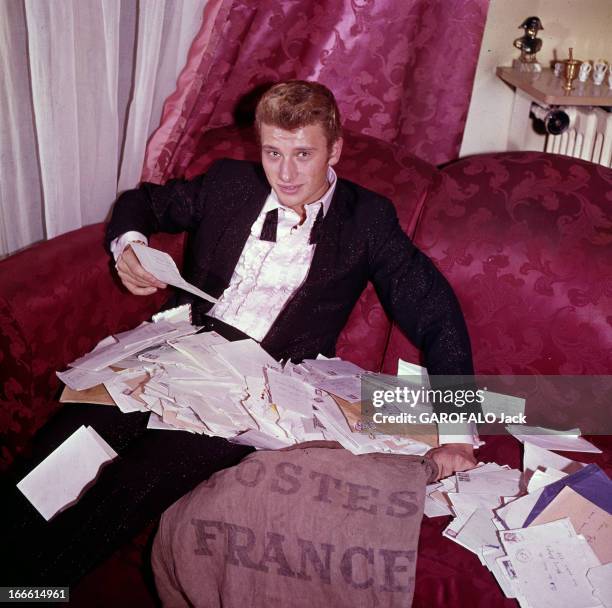 Rendezvous With Johnny Hallyday. France- Portrait de Johnny HALLYDAY, souriant, assis dans un canapé rouge carmin, vêtu d'un costume noir et chemise...