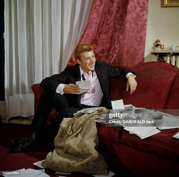 Rendezvous With Johnny Hallyday. Portrait de Johnny HALLYDAY, souriant, assis dans un canapé rouge carmin, vêtu d'un costume noir et chemise à...