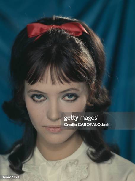 Anna Karina Poses In Studio. France- Portrait studio d'Anna KARINA, vêtue d'un chemisier à dentelle blanche et coiffée d'un serre-tête à noeud rouge...