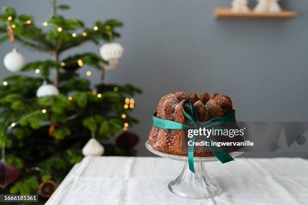 christmas chocolate cake with a tied bow on a table in front of christmas tree - pound cake stock pictures, royalty-free photos & images