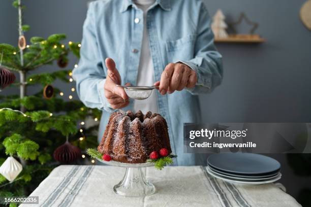 man sprinkling powdered sugar over christmas chocolate cake - cakes stockfoto's en -beelden