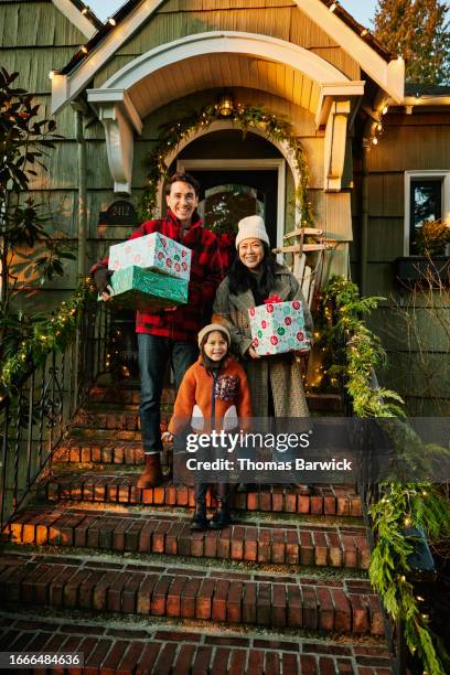 wide shot family holding christmas presents on front steps of home - long coat stock pictures, royalty-free photos & images