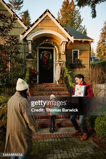 Wide shot girl carrying Christmas presents down front steps of home