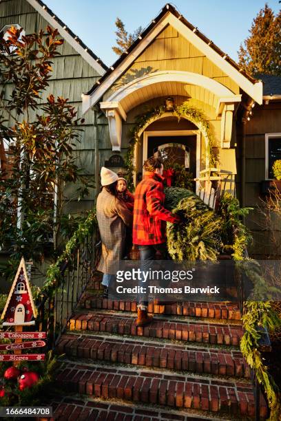 wide shot father carrying christmas tree up front steps of home - long coat stock pictures, royalty-free photos & images