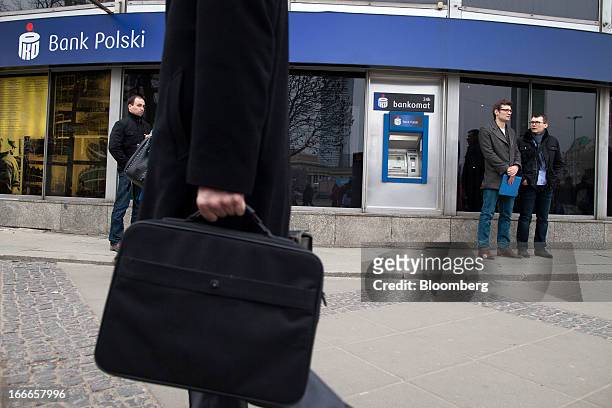 Pedestrians pass an automated teller machine outside a PKO Bank Polski SA bank branch in Warsaw, Poland, on Thursday, April 11, 2013. Poland's...