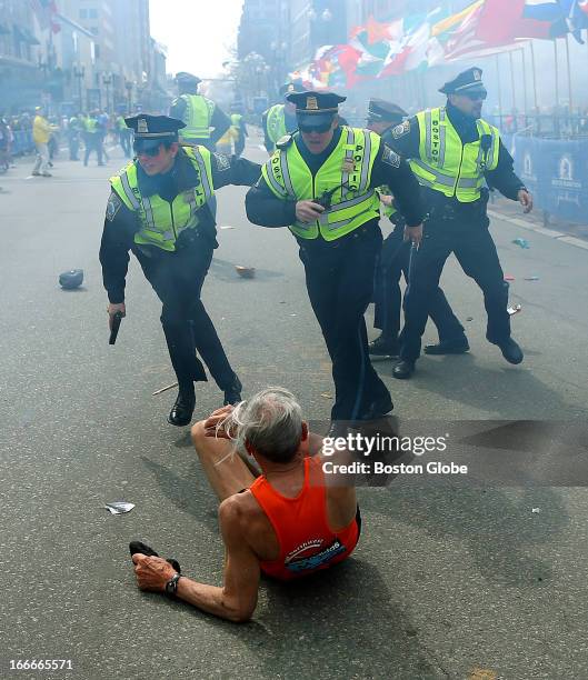 Police officers with their guns drawn hear the second explosion down the street. The first explosion knocked down 78-year-old US marathon runner Bill...