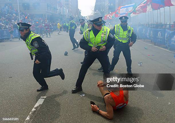 Police officers with their guns drawn hear the second explosion down the street. The first explosion knocked down 78-year-old US marathon runner Bill...