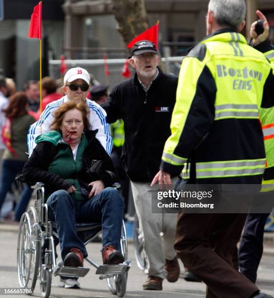 First responders transport an injured woman in a wheelchair where two explosions occurred along the final stretch of the Boston Marathon on Boylston...