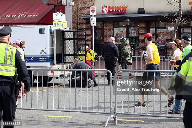 Members of the bomb squad investigate a suspicious item on the road as runners pass near Kenmore Square after two bombs exploded during the 117th...