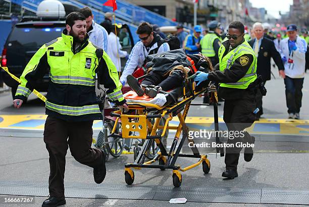 Person who was injured in the first explosion is wheeled across the finish line of the Boston Marathon.
