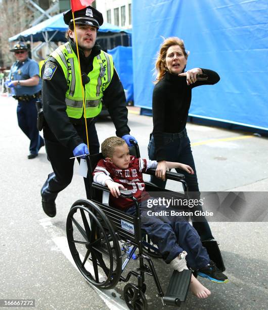 An injured boy is pushed in a wheelchair by a Boston police officer at the scene of the first explosion near the finish line of the Boston Marathon.