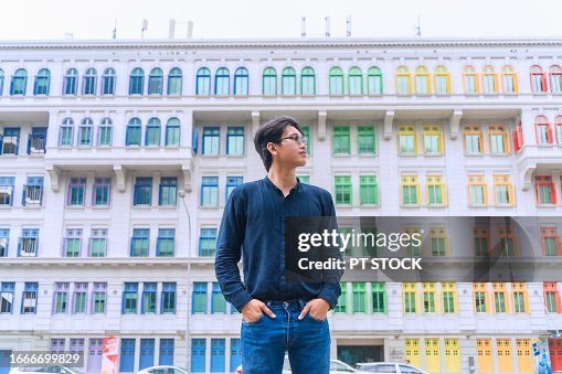 A male tourist wearing sunglasses stands on the street behind colorful buildings in Singapore.