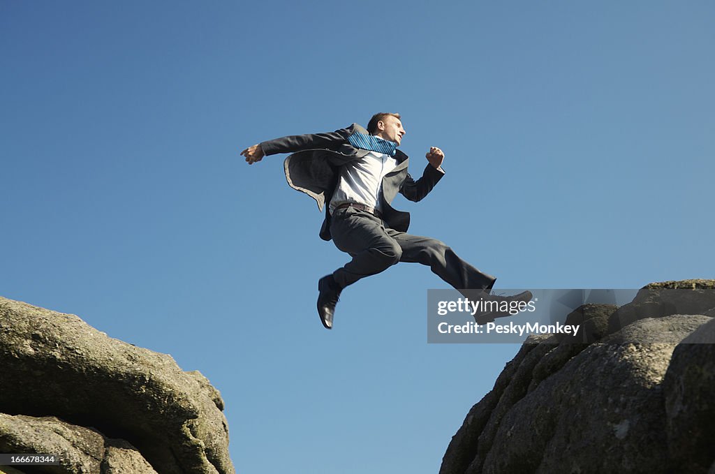Energetic Young Man Businessman Jumping into Blue Sky between Rocks