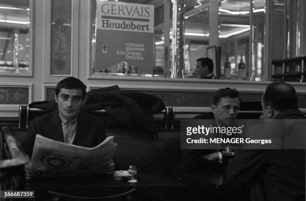 Actor Charles Denner. A Paris, en 1963, l'acteur Charles DENNER, lisant son journal dans un café, au dessus d'une publicité pour les glaces Gervais..