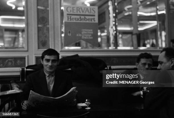 Actor Charles Denner. A Paris, en 1963, l'acteur Charles DENNER, souriant, lisant son journal dans un café, au dessus d'une publicité pour les glaces...