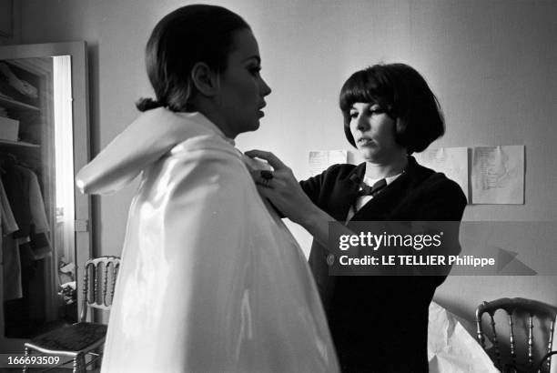 Victoire Fashion Show. Le 25 mai 1965, une femme non identifiée habille une mannequin qui porte un manteau avec une capuche, clairs, en vinyle, pour...