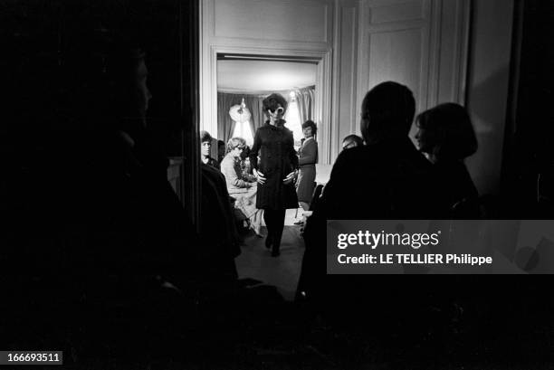 Victoire Fashion Show. Le 25 mai 1965, une mannequin porte un manteau long et des lunettes de soleil, dans un salon devant des gens qui prennent des...