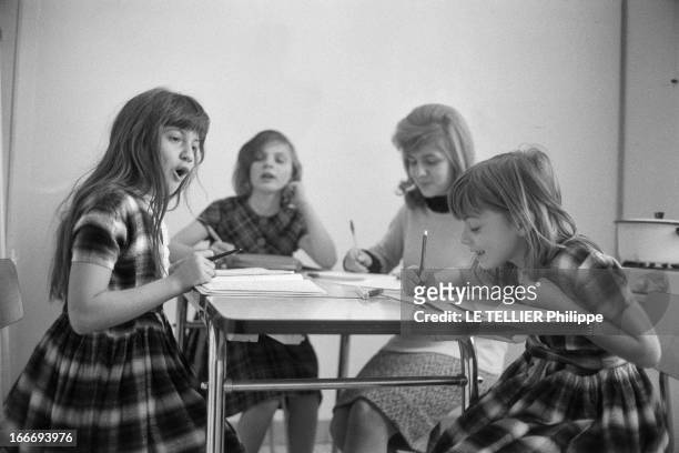 Patricia Gozzi. Portrait de la jeune actrice Patricia GOZZI, faisant ses devoirs, assise à une table en compagnie de trois fillettes. Elle porte une...