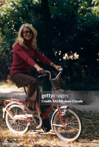 Rendezvous With Catherine Deneuve. Attitude souriante de Catherine DENEUVE en pantalon à franges faisant du vélo sur un chemin forestier..