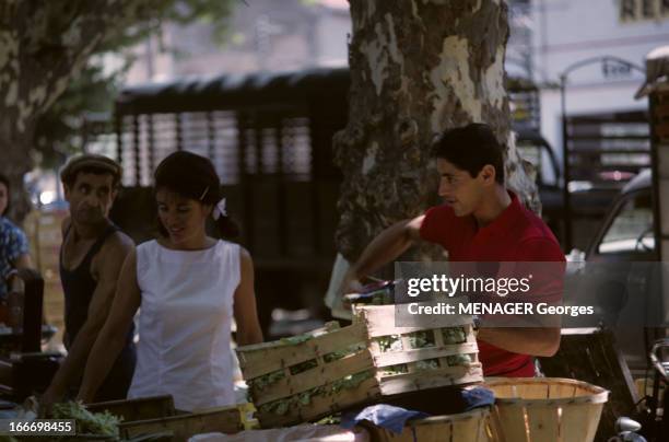 Vips On Holiday In Saint-Tropez. Saint-Tropez - juillet 1963 - Le chanteur Sacha DISTEL en polo rouge, faisant son marché en compagnie de son épouse...