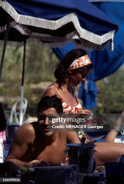 Vips On Holiday In Saint-Tropez. Saint-Tropez - juillet 1963 - Le chanteur Sacha DISTEL allongé torse nu sous un parasol, devant son épouse la...