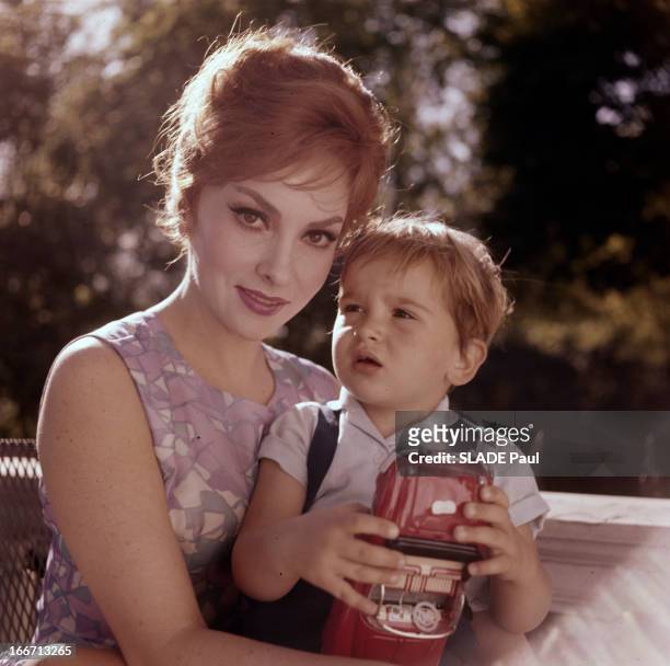 Gina Lollobrigida And Son Milko. Portraits en extérieurs de Gina LOLLOBRIGIDA, en robe tenant son fils Milko, jouant avec une voiture modèle réduit,...