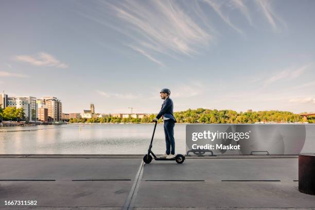 side view of businessman commuting through electric push scooter on promenade against sky - scooter city fotografías e imágenes de stock