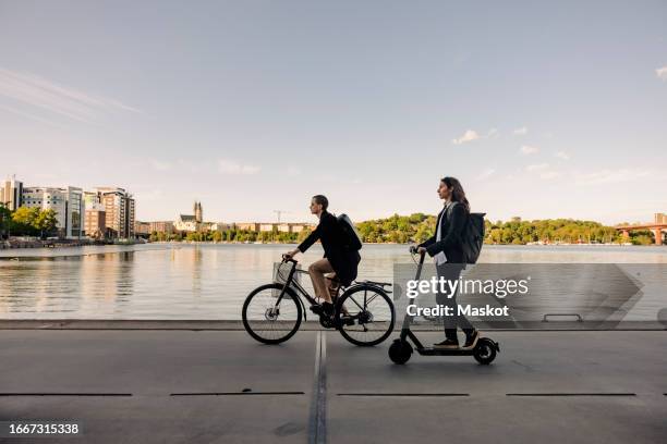 business people riding electric scooter and bicycle on promenade against sky - sustainable transportation stock pictures, royalty-free photos & images