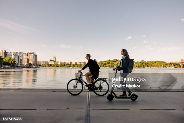 business people riding electric scooter and bicycle on promenade against sky - trotinete imagens e fotografias de stock