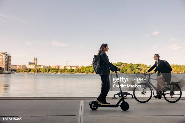 businesswoman and non-binary person riding cycle and electric push scooter on promenade - non motorised vehicle stock pictures, royalty-free photos & images