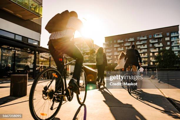 business people commuting through bicycles on promenade at sunset - sustainable transportation stock pictures, royalty-free photos & images