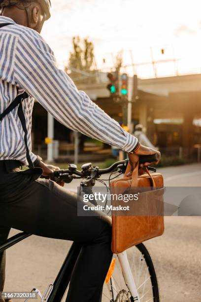 businessman with laptop bag hanging on bicycle handle while waiting at stoplight - laptoptasche stock-fotos und bilder