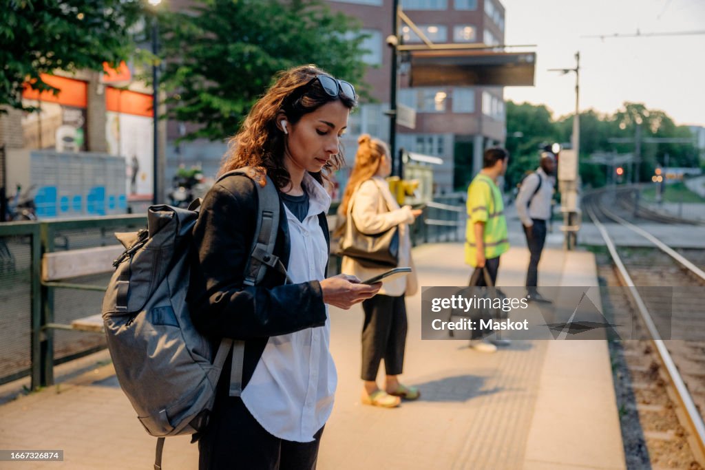 Businesswoman carrying backpack and using smart phone while waiting for tram at station