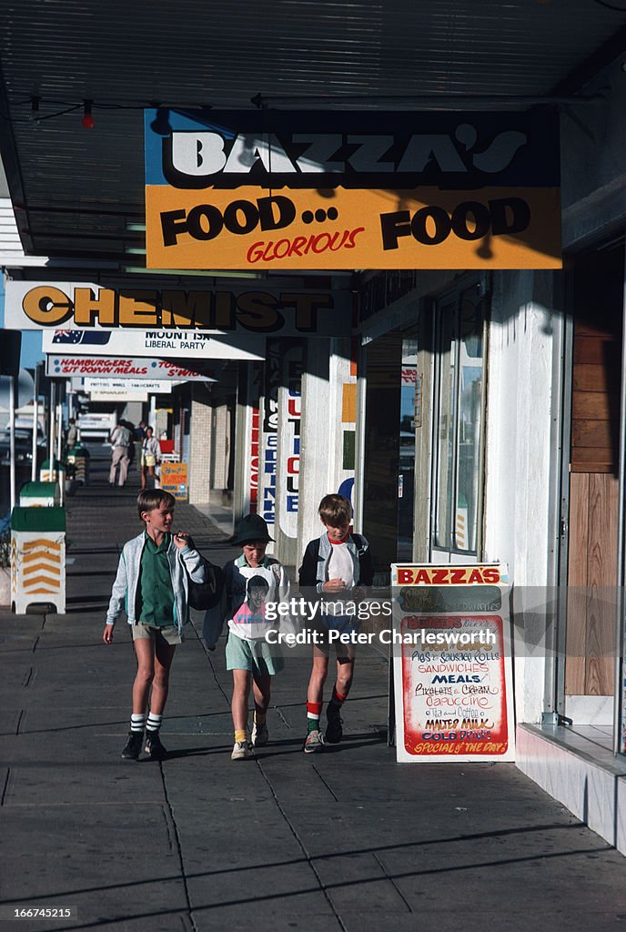 Three boys walk down the pavement or sidewalk on a small...