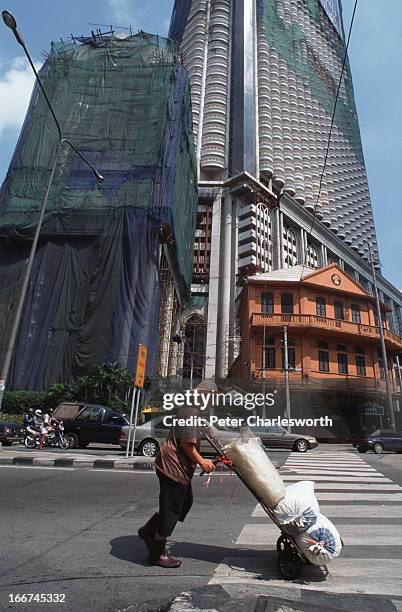 Man pushes a trolley past a vast real estate development. This half finished high rise office and apartment block stands on a corner of a busy...