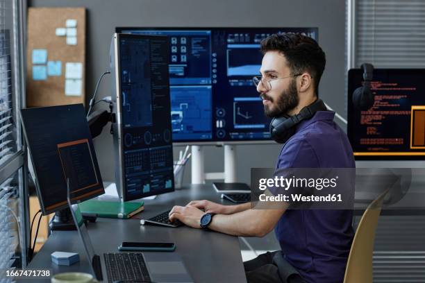 young computer programmer with wireless headphones coding on desktop pc - web programmer stock pictures, royalty-free photos & images