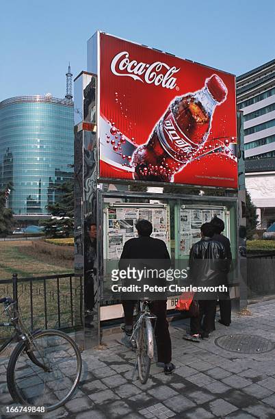 Passersby catch up on the latest news with newspapers posted on a notice board under a Coca-Cola sign on Jianguomenwai Avenue. Newspapers and...