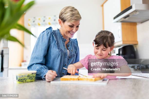 girl spreading butter on bread by mother standing in kitchen - girl making sandwich stock pictures, royalty-free photos & images