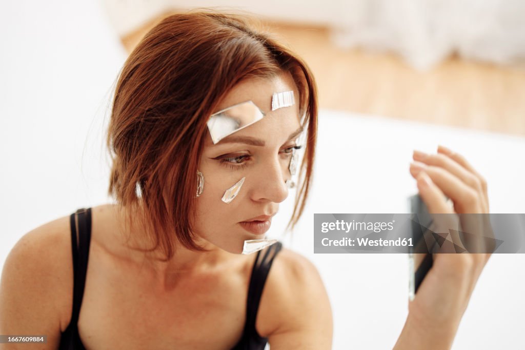 Woman with broken mirror pieces on face at home