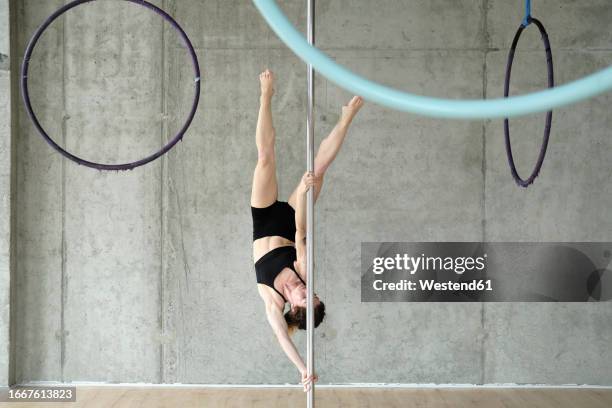 woman practicing gymnastics on pole in front of concrete wall - stangentänzerin stock-fotos und bilder