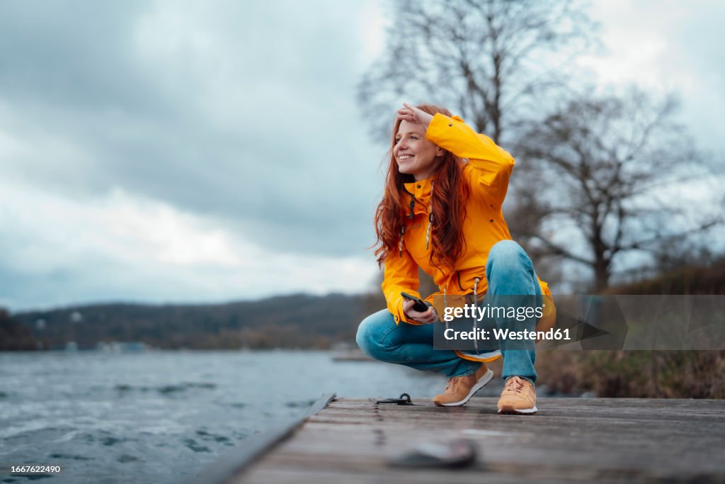 Smiling woman squatting on pier by lake