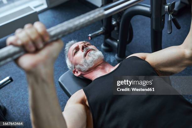 mature man doing bench press in health club - entrenamiento de fuerza fotografías e imágenes de stock