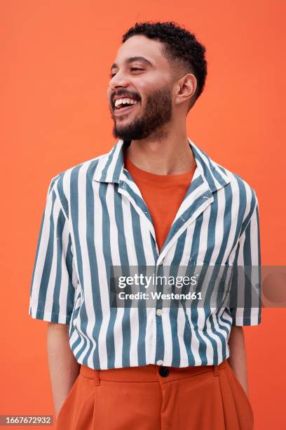 smiling man wearing striped shirt standing against orange background - estilo imagens e fotografias de stock