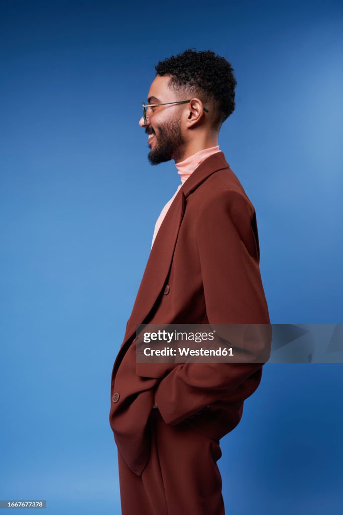Smiling man wearing brown blazer standing against blue background