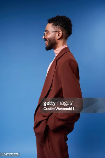 smiling man wearing brown blazer standing against blue background - brown suit stock pictures, royalty-free photos & images