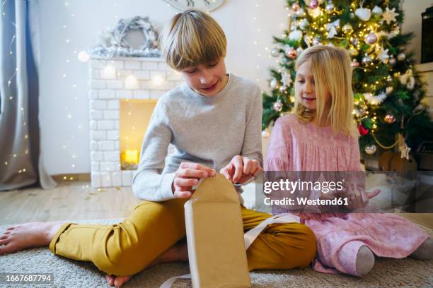 boy opening christmas present by sister in living room - open day 13 stock pictures, royalty-free photos & images