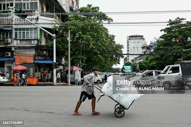 Man pushing a cart crosses a street in the city centre of Yangon on September 15, 2023.