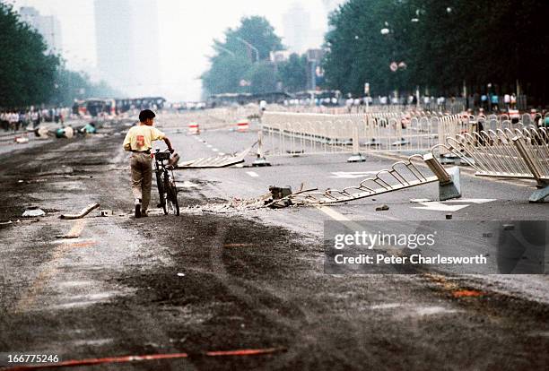 At the end of the pro-democracy protests in China, a lone cyclist walks past street barriers on Chang'an Avenue, crushed by Chinese Army tanks during...