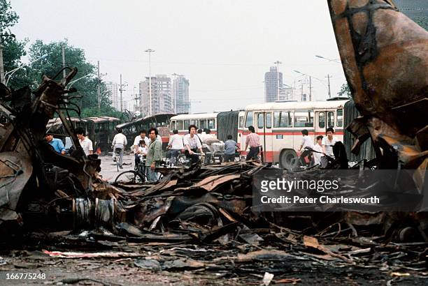 At the end of the pro-democracy movement in China, onlookers examine destroyed buses, once barricades, that were run over by Chinese Army tanks...