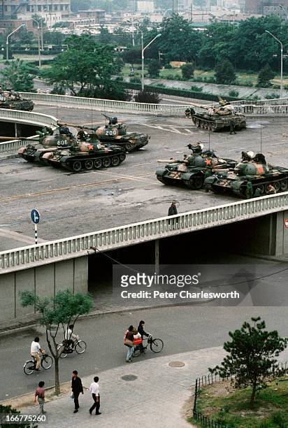 At the end of the pro-democracy movement in China, pedestrians and cyclists pass underneath a group of Chinese Army tanks. The tanks are blocking an...